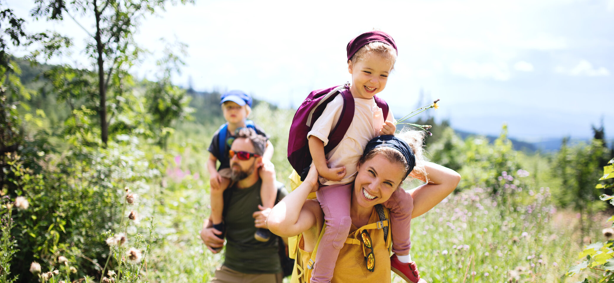 Eine Familie in der Natur, die Mutter trägt ein Kind auf den Schultern | © Halfpoint / Adobe Stock